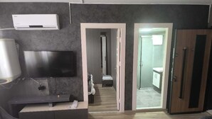 A modern living room with a flat-screen TV, a sofa, and a coffee table. There is a doorway leading to a bathroom with a glass shower enclosure. - Elite Residence PLUS (Izmir)