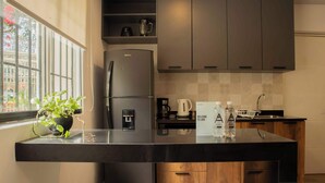Eine moderne Küche mit integriertem Kühlschrank, einer Kaffeemaschine und einem Wasserspender. Auf der Arbeitsplatte liegen ein Willkommensschild und zwei Wasserflaschen.