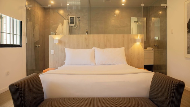A modern hotel room with a large bed, a glass-enclosed shower area, and a wooden headboard.