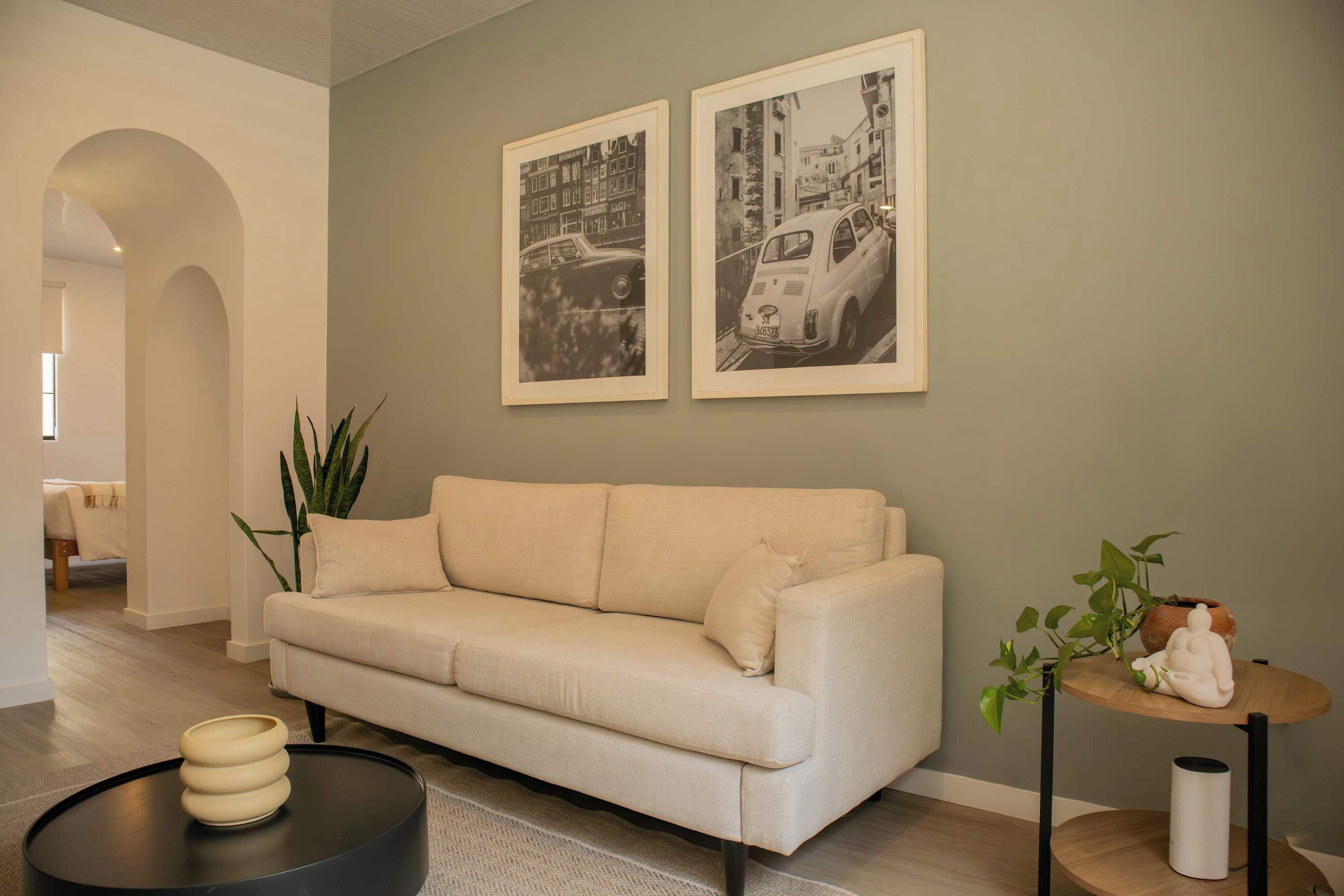 A modern living room with a beige sofa, a round black coffee table, and a small wooden side table with a plant.