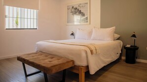 A bedroom with a bed, a bench, a window with bars, a framed picture on the wall, and a lamp on a side table. - w* | Exceptional 1BR w/ Terrace in Miraflores (Miraflores)