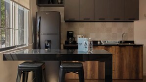 A modern kitchen with a black countertop, wooden cabinets, a refrigerator, and a window providing natural light. - w* | Exceptional 1BR w/ Terrace in Miraflores (Miraflores)