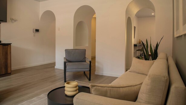 A living room with a beige sofa, a grey armchair, and a coffee table. There are three arched doorways leading to other rooms. - w* | Exceptional 1BR w/ Terrace in Miraflores (Miraflores)