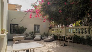 An outdoor patio with tables and chairs, a small seating area with cushions, and a wall adorned with plants and flowers.