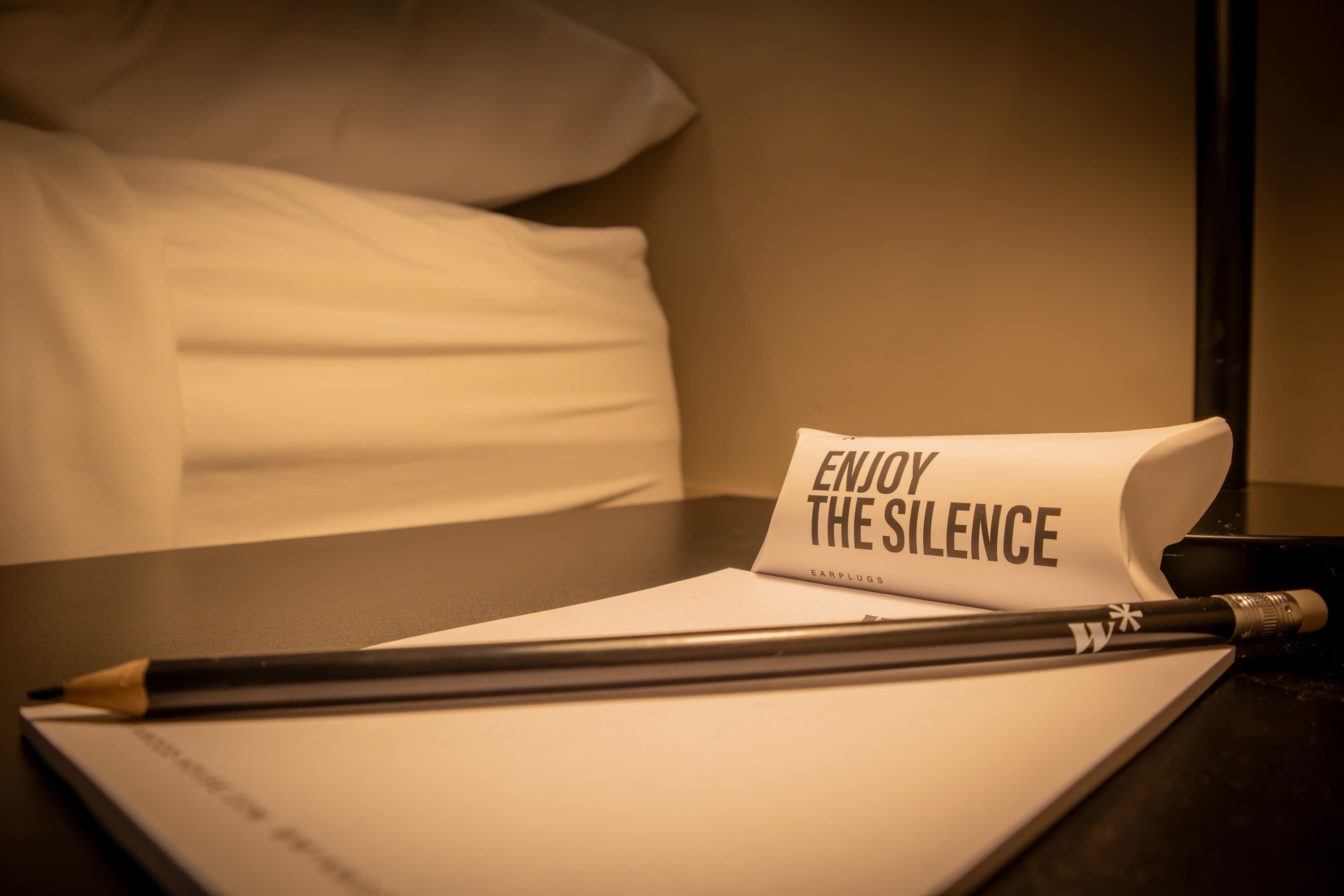 A neatly made bed with a pillow and a rolled-up note on a bedside table.