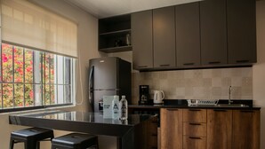 A modern kitchen with a black island, wooden cabinets, and a window with a view of red flowers.