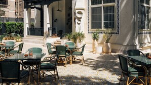 An outdoor seating area with wicker furniture and potted plants, a balcony with a black railing, and a building with decorative moldings and large windows. - Private fully serviced villa in Maadi, with a private pool, kitchen and garden. (Cairo Governorate)