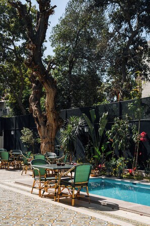 An outdoor seating area with a pool, surrounded by greenery and a large tree. - Private fully serviced villa in Maadi, with a private pool, kitchen and garden. (Cairo Governorate)