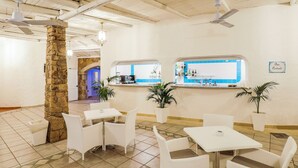 A restaurant with white furniture, stone pillars, and a bar area with a blue counter. - Nicolaus Club Li Cucutti  (Agrustos)