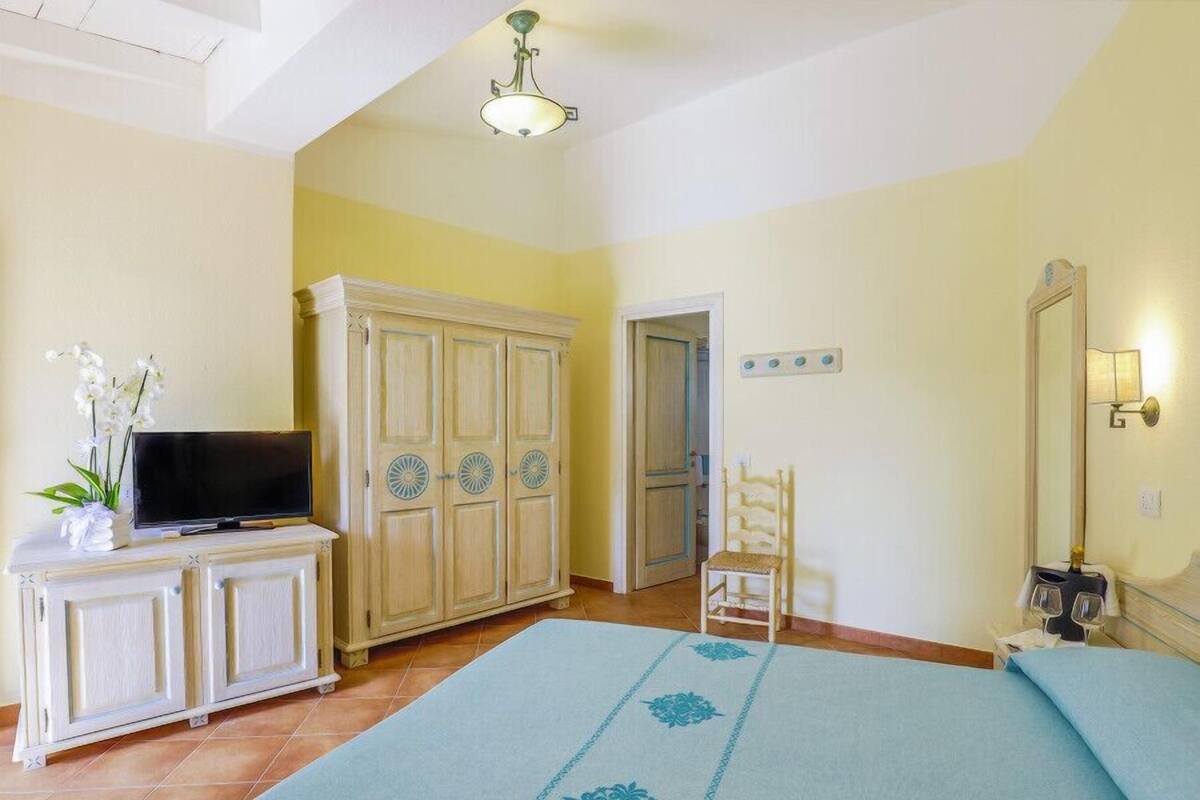 A bedroom with a bed, a TV on a cabinet, a wardrobe, a chair, and a mirror.