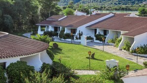 A row of white buildings with red-tiled roofs, surrounded by greenery and a mountainous backdrop. - Nicolaus Club Li Cucutti  (Agrustos)