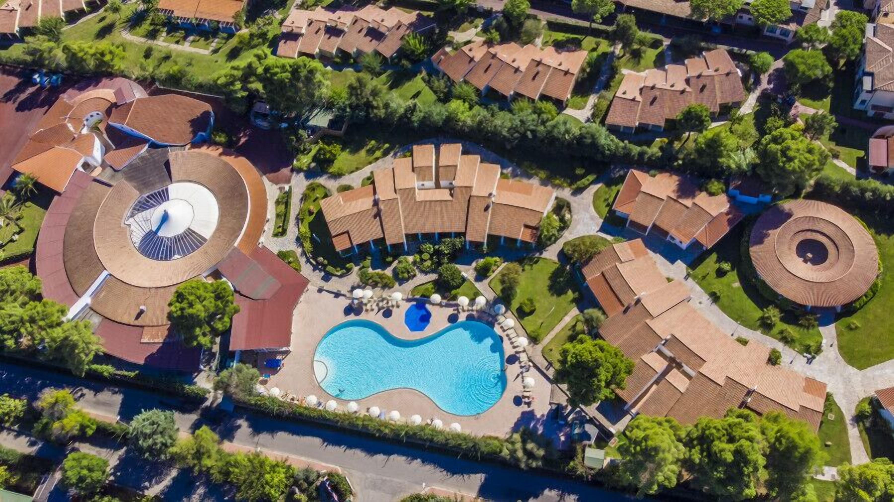 An aerial view of a resort with a central swimming pool, multiple circular structures, and surrounding villas.