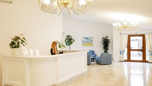 A reception area with a white reception desk, a chandelier, and several potted plants. - Nicolaus Club Li Cucutti  (Agrustos)