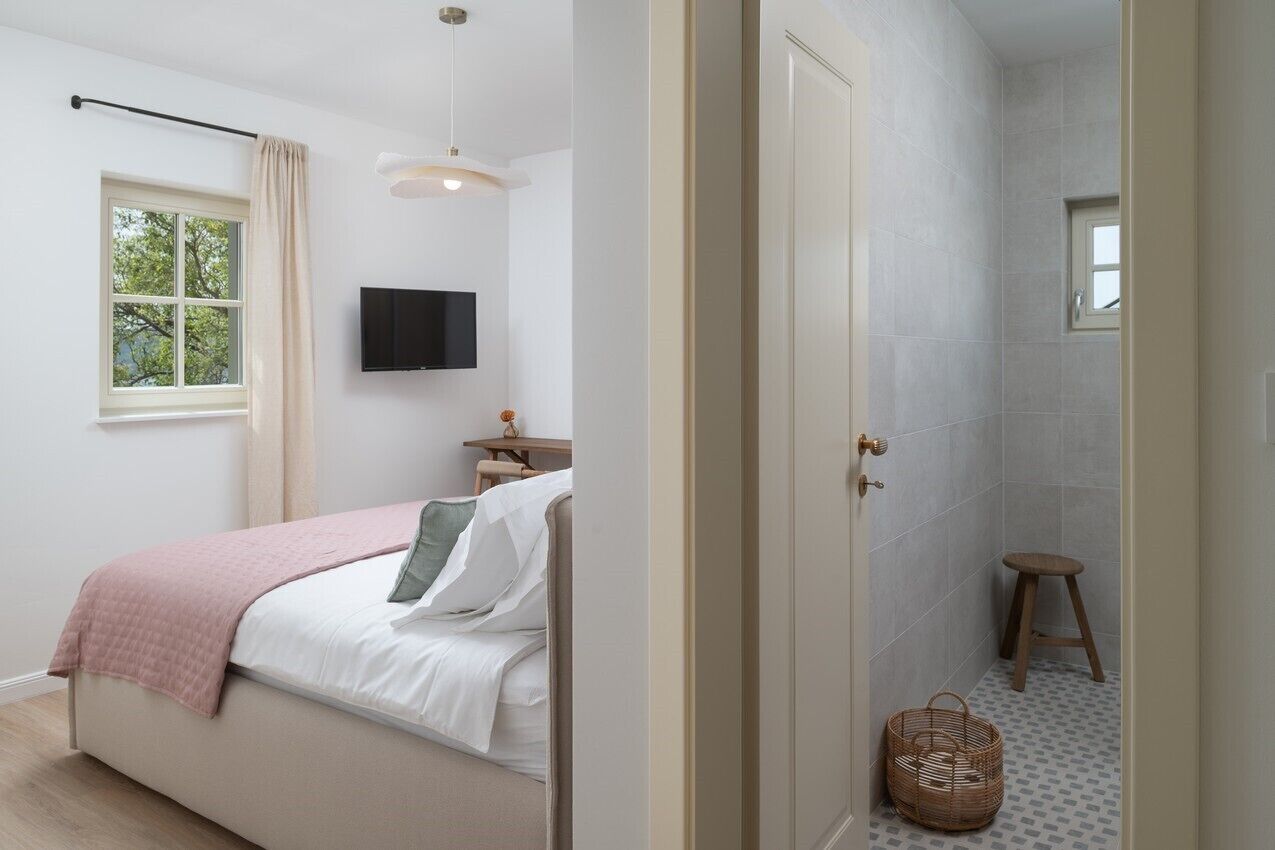 A bedroom with a bed, a bedside table, a TV, and a window with curtains.