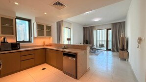 A modern kitchen with a dishwasher, a coffee machine, and a dining area with a table and chairs. - Dancenter Luxury 2 BR at Creek Side (Dubai)