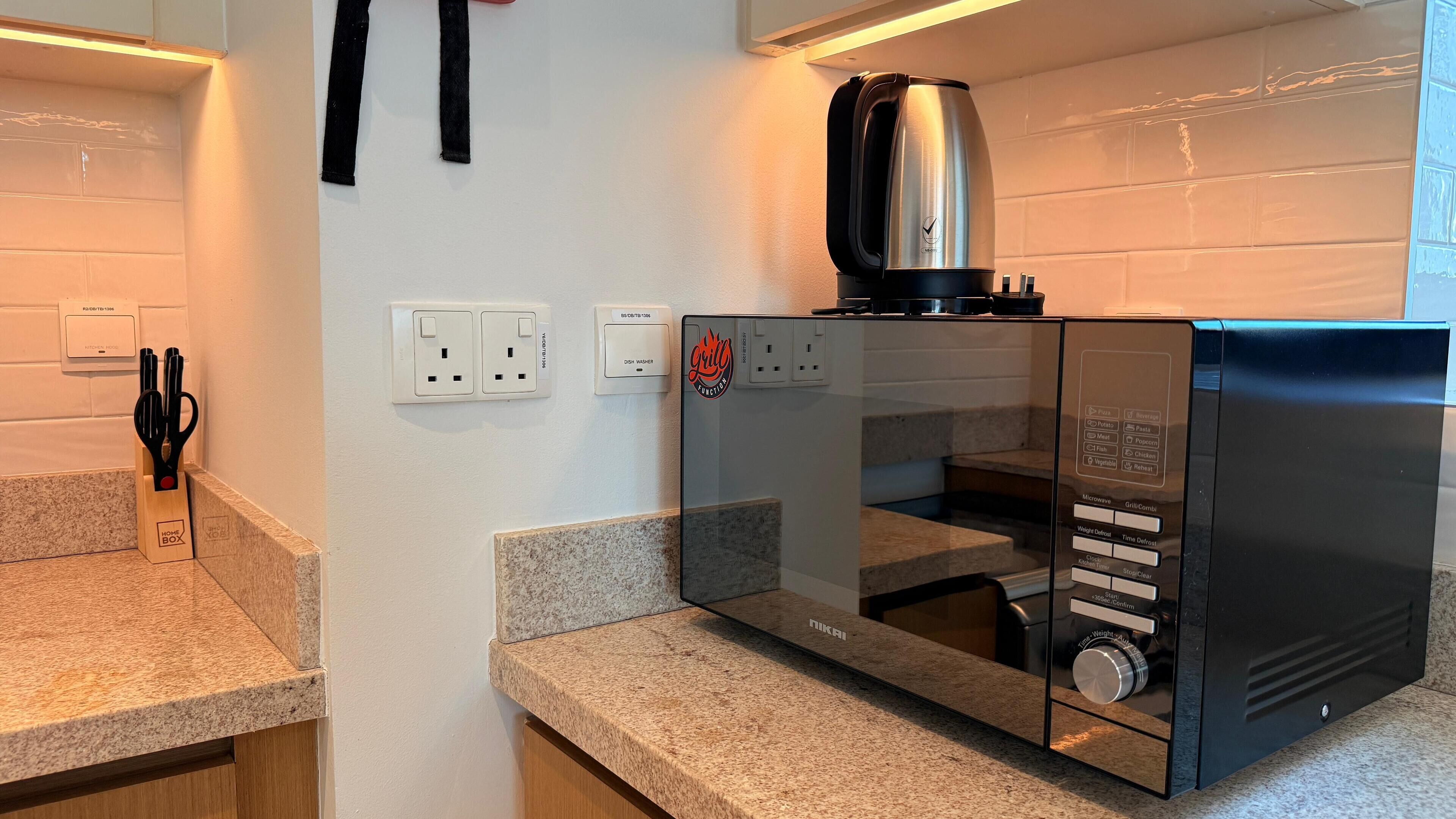 Eine Küche mit integriertem Mikrowellenherd, einer Kaffeemaschine und einem Geschirrspüler. An der Wand befinden sich zwei Steckdosen und ein Mehrfachsteckdosenleiste.
