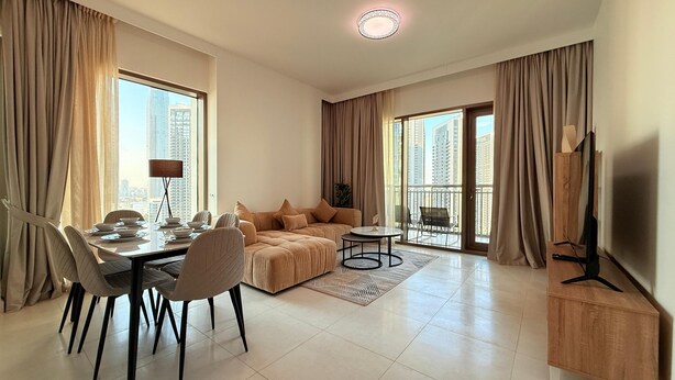 A modern living room with a dining area, large windows, and a flat-screen TV. - Dancenter Luxury 2 BR at Creek Side (Dubai)