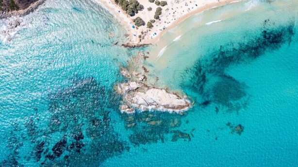 An aerial view of a beach with clear turquoise waters, sandy shore, and scattered trees. - Nicolaus Prime Villas   (Castiadas)