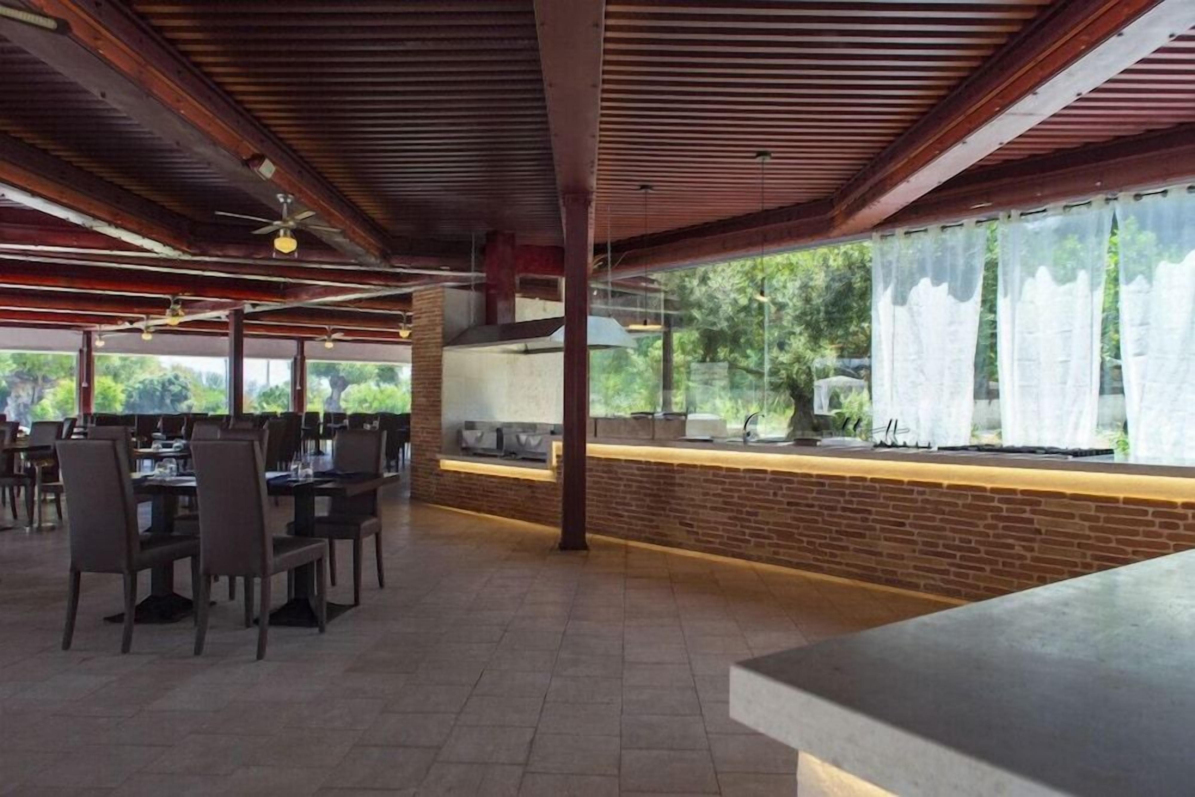 An indoor dining area with brick walls, wooden ceiling beams, and a long counter with a view of greenery outside.