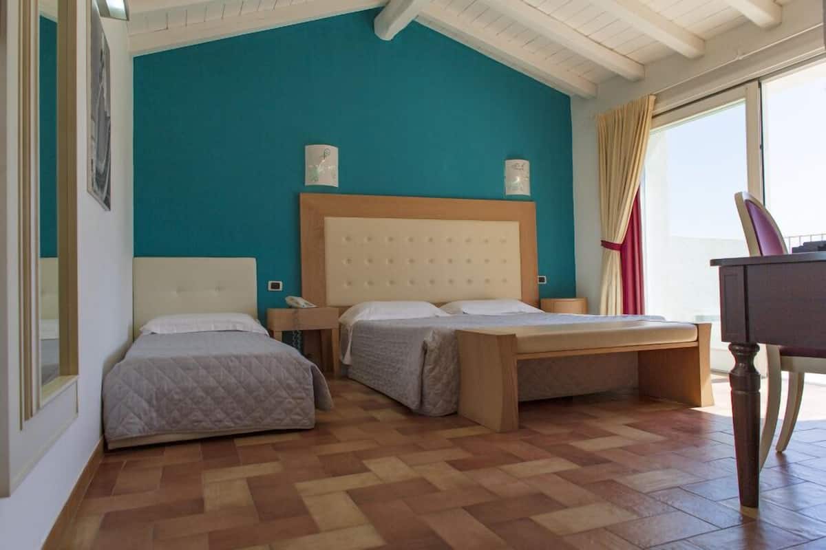 A hotel room with two beds, a wooden headboard, a desk, and a window with curtains.