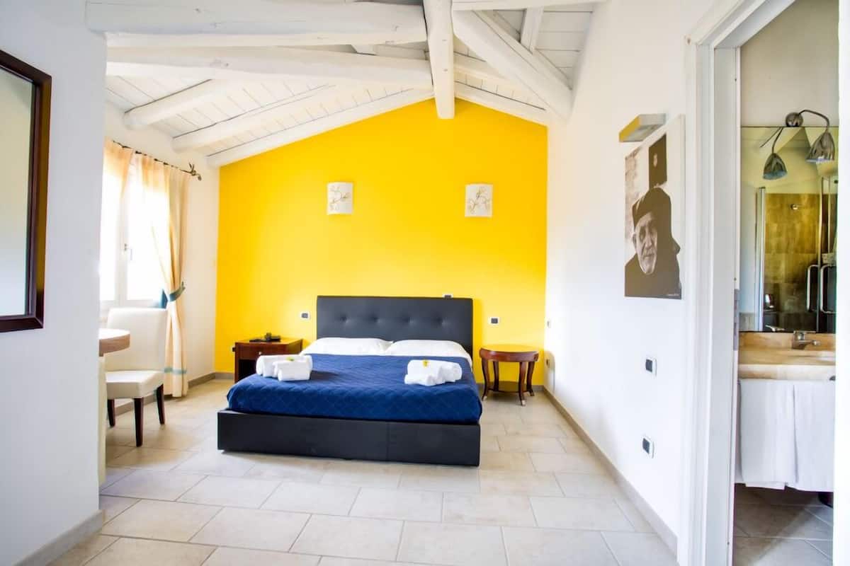 A bedroom with a bed, a chair, a nightstand, and a bathroom visible through an open door.