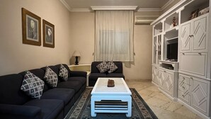A living room with a black sofa, patterned cushions, a white coffee table, and a cabinet with a television. - Cozy 2-bedroom apartment in serene Cairo (Cairo Governorate)