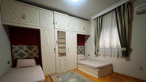 A bedroom with two single beds, a wardrobe, and a small window with curtains. - Cozy 2-bedroom apartment in serene Cairo (Cairo Governorate)