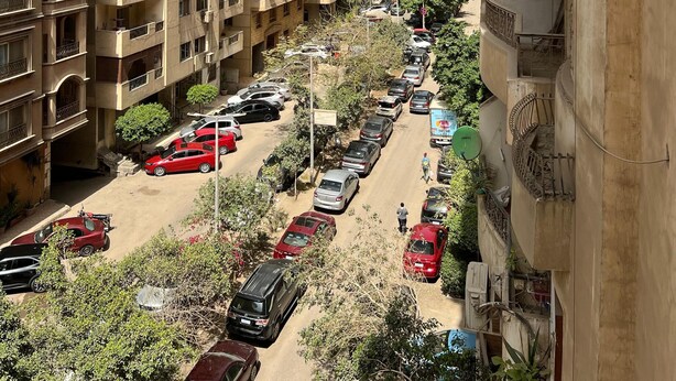 A multi-story residential building with balconies, a parking lot, and a clear sky. - Cozy 2-bedroom apartment in serene Cairo (Cairo Governorate)