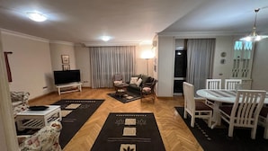 A living room with a flat-screen TV, a sofa, a coffee table, and a dining area with a table and chairs. - Cozy 2-bedroom apartment in serene Cairo (Cairo Governorate)