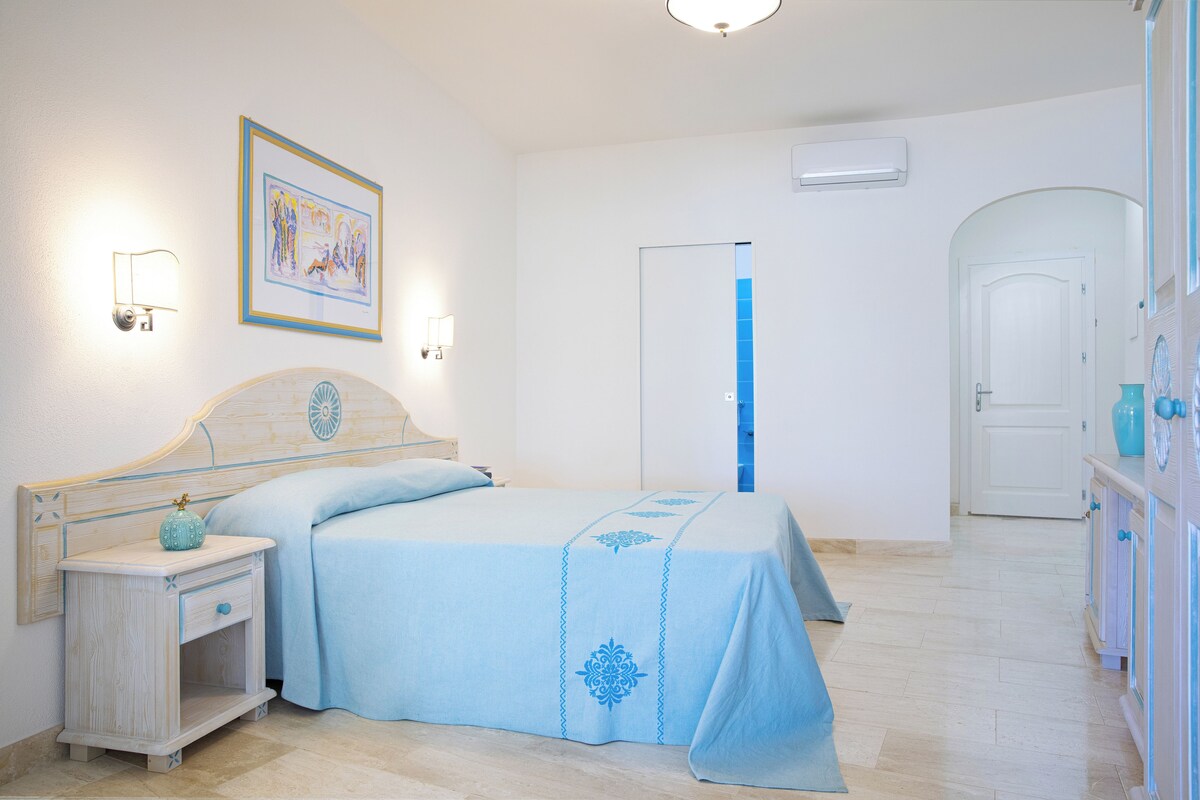 Un dormitorio con cama, mesita de noche, luces en la pared, una puerta y cómoda.