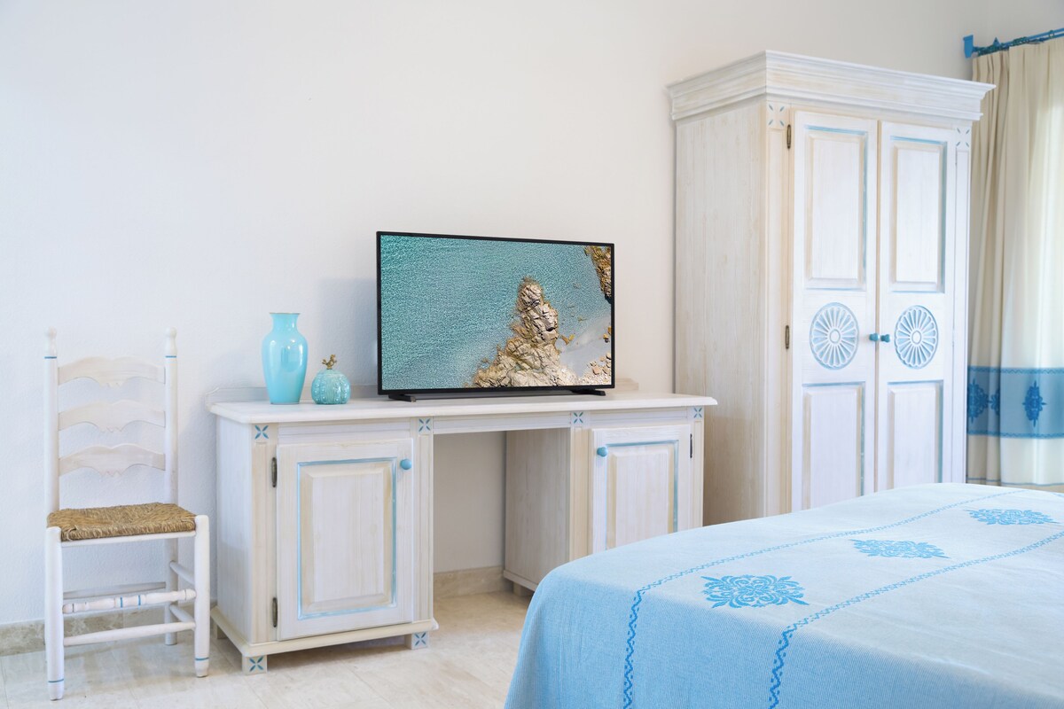 Un dormitorio con una cama, un televisor sobre un aparador blanco, una silla y un armario.