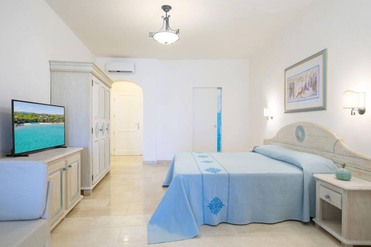A hotel room with a bed, a TV, a wardrobe, and a bathroom visible through an open door.