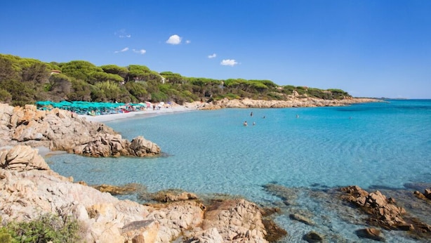 Una playa costera con aguas turquesas cristalinas, costas rocosas y abundante vegetación verde.