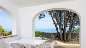 Un patio con mesa y sillas blancas, un muro de piedra y vista al mar.