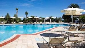 Una piscina con sillones de descanso y sombrillas, rodeada de palmeras.