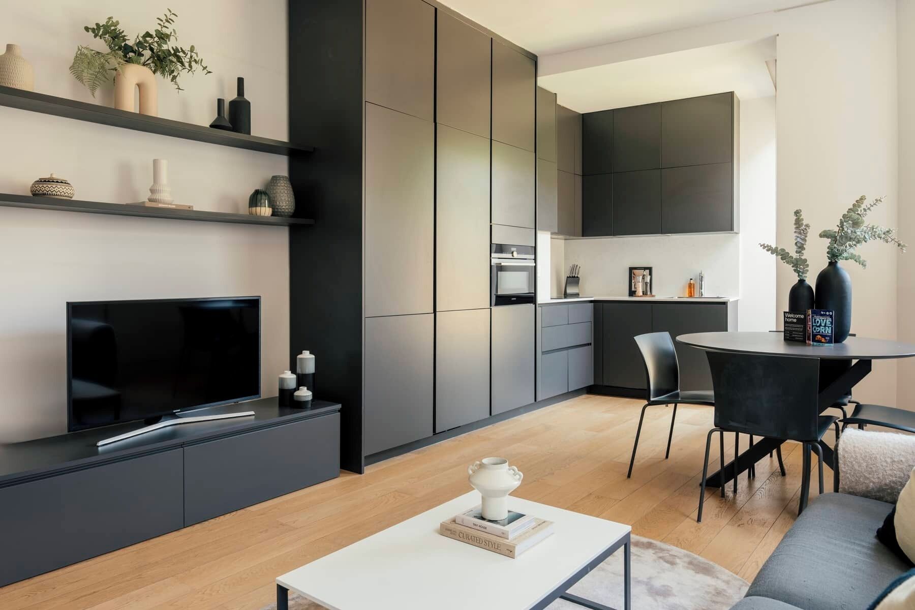 En moderne stue med et fladskærms-tv, et sofabord med bøger, en sofa og et spiseområde med et bord og stole.