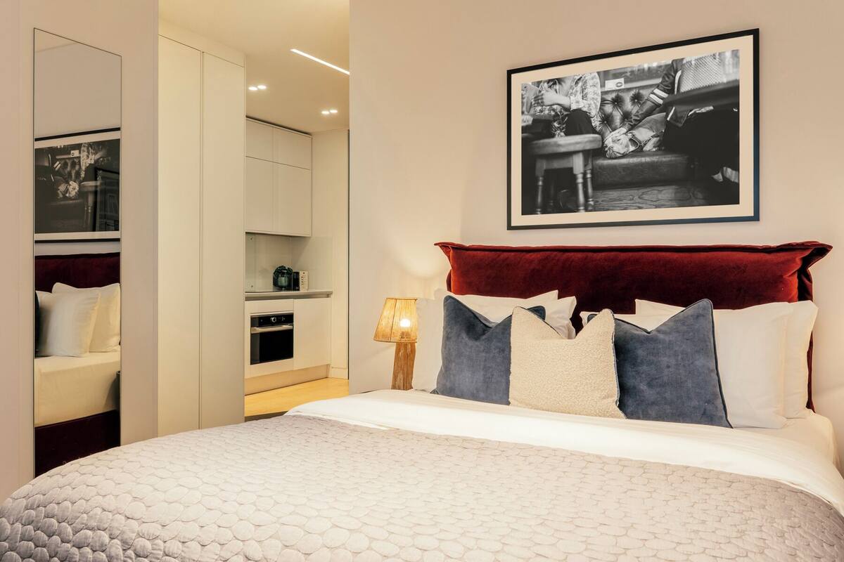 A bedroom with a bed, a red headboard, a nightstand, a lamp, and a framed picture on the wall.