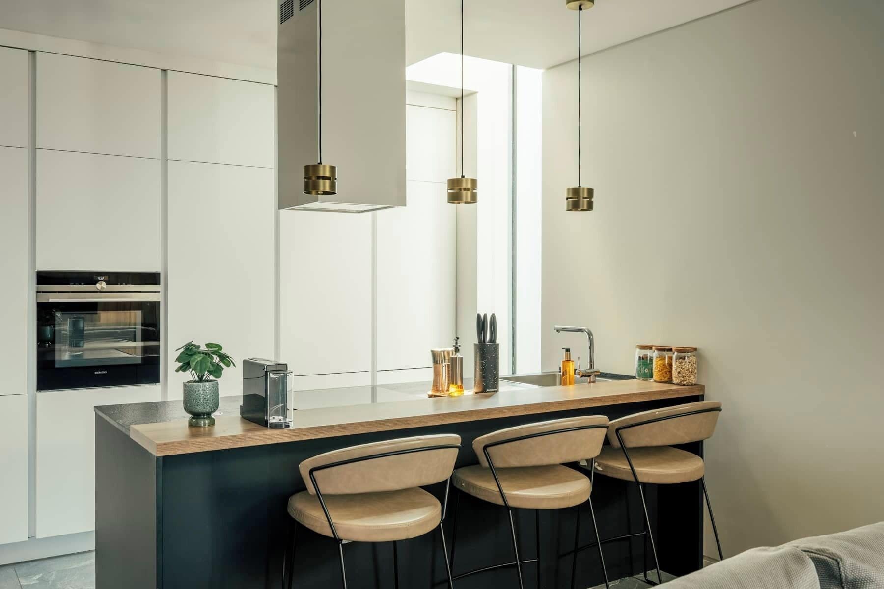 A modern kitchen with a central island, bar stools, a built-in oven, and pendant lighting.