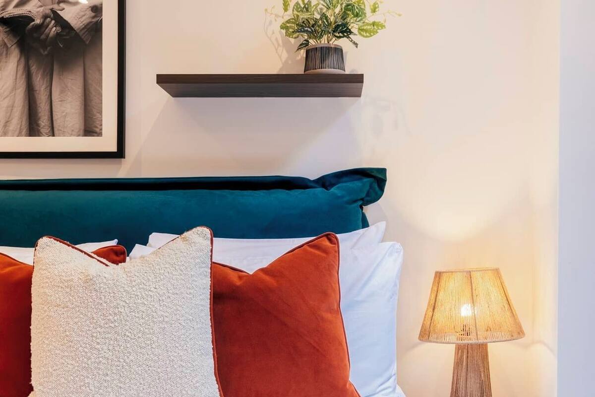 A neatly made bed with patterned bedding, a teal headboard, and a bedside lamp.