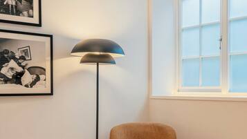 A bedroom with a bed, a chair, a floor lamp, a small table, and a window with frosted glass.
