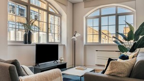 Una sala de estar con televisor, sofá, mesa de centro y ventanas amplias.