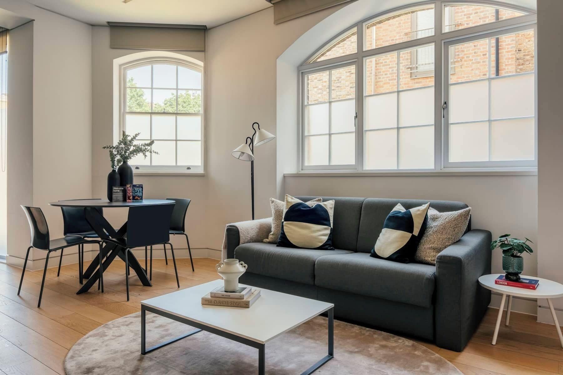 A modern living room with a grey sofa, a coffee table, and a dining area with a table and chairs.