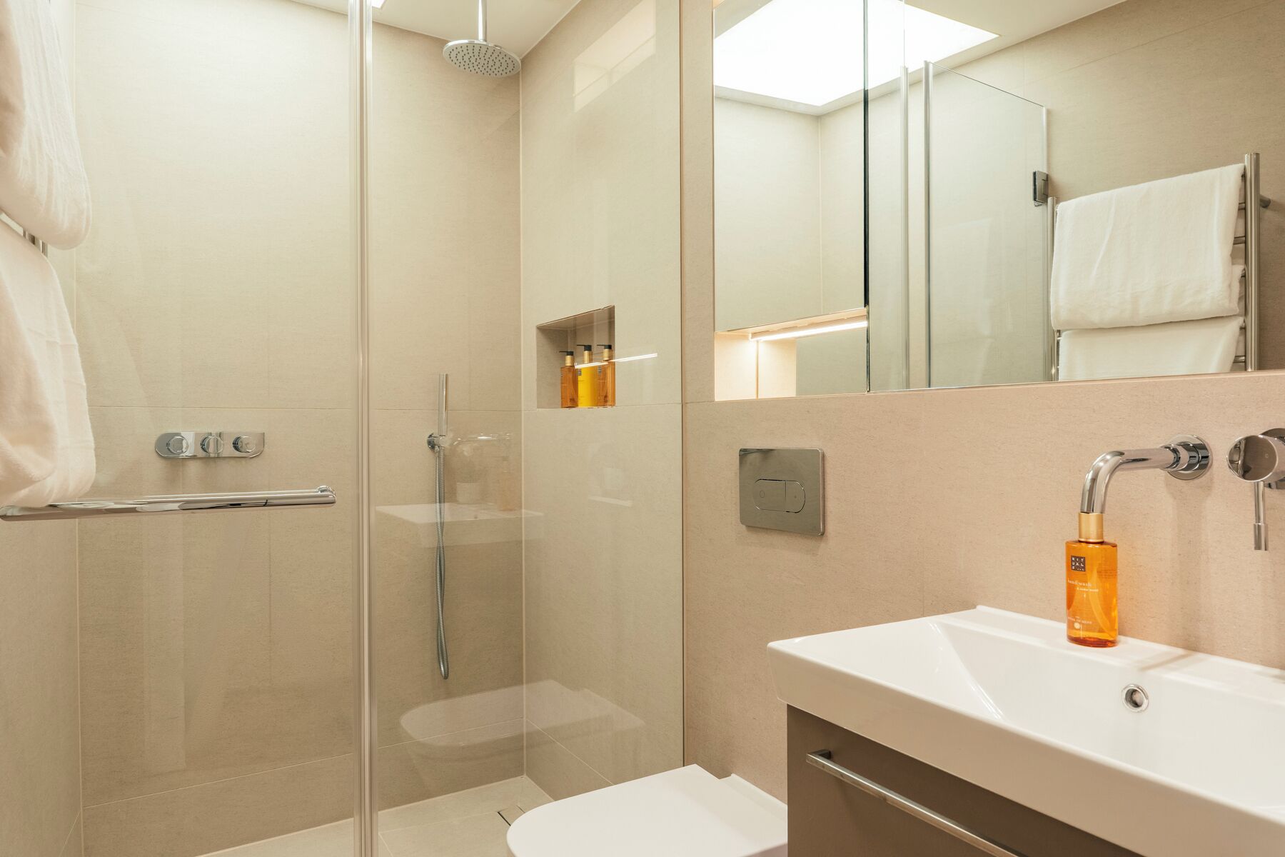 A modern bathroom with a glass-enclosed shower, a white sink, and a mirror.