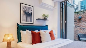 Una cama bien hecha con almohadas blancas y rojas, un cabecero color verde azulado y una lámpara de bambú sobre una mesita de noche.