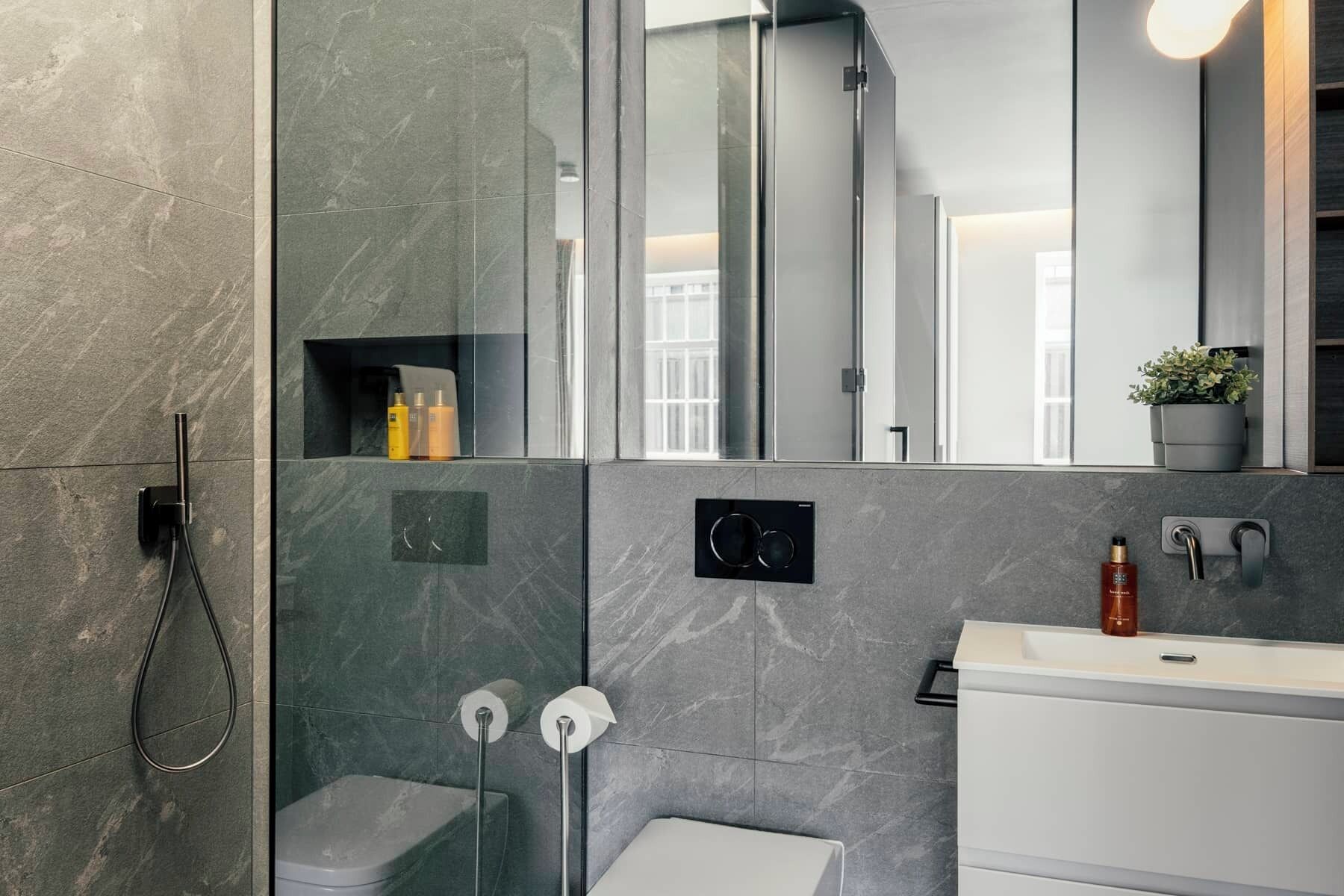 A modern bathroom with a glass shower enclosure, a toilet, and a sink with a mirror above.