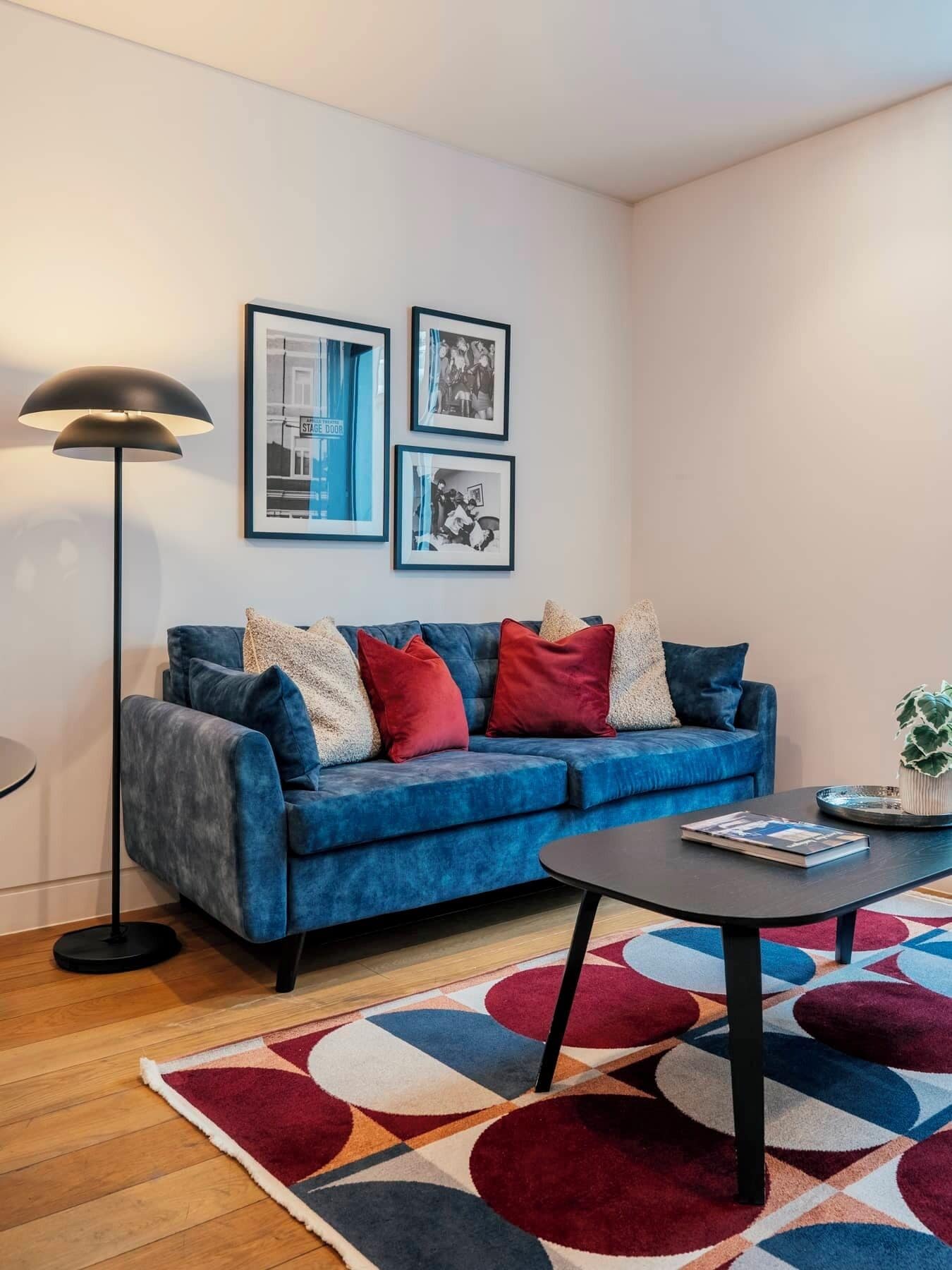 A modern living room with a blue sofa, a round coffee table, a floor lamp, and a colorful rug.