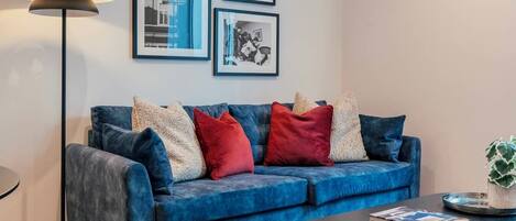 A modern living room with a blue sofa, a round coffee table, a floor lamp, and a colorful rug.