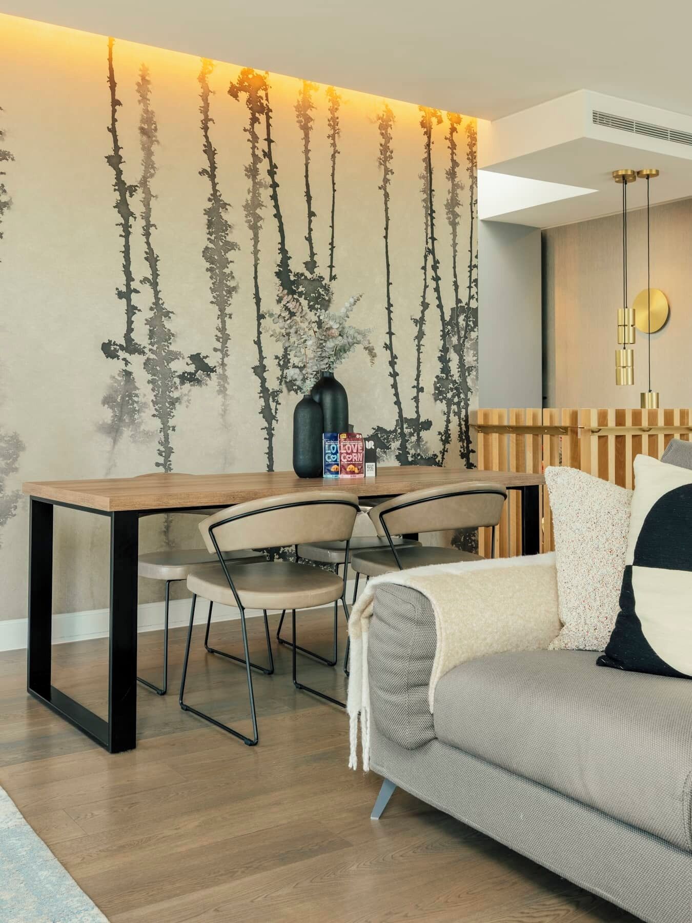 Una sala de estar moderna con una mesa de comedor de madera, dos sillas, un sofá y una pared decorativa con elementos verticales.