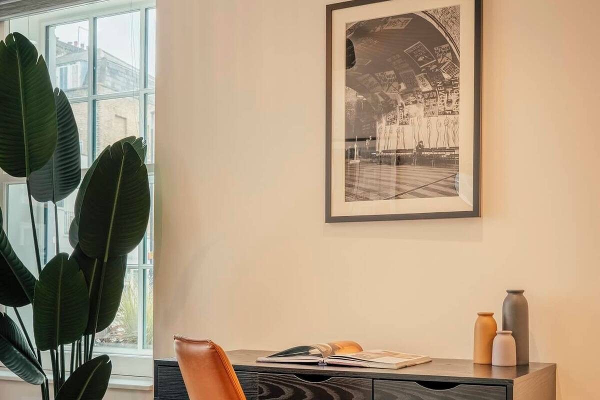 A modern room with a desk, chair, potted plant, and a framed picture on the wall.