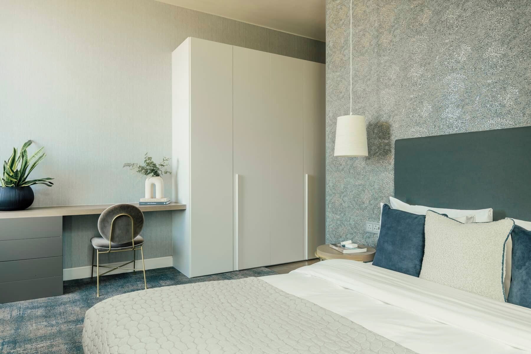 Et hotelværelse med seng, skrivebord, stol, skab og væglampe.